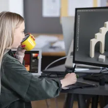 Fiatal lány ül egy monitor előtt és 3d grafikát tervez